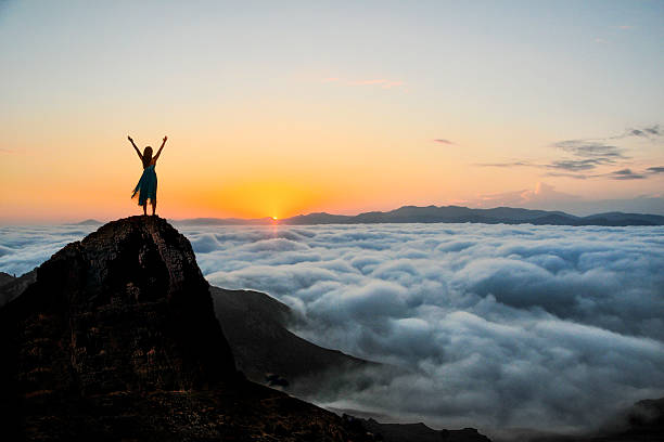 Woman enjoys on top of a cliff above the sea of clouds at sunset.